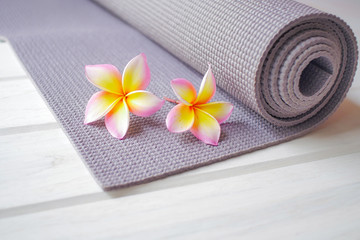 Plumeria flowers and purple yoga mat on a white wood floor