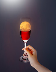 Hand hold the wine  onto the red moon - Red moon concept.