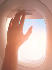 Passenger's hand closing the window shade on a modern airplane.