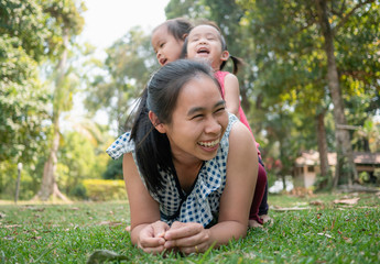 Obraz premium Happy Asian young mother lying on grass and daughters sitting on her back in the park.