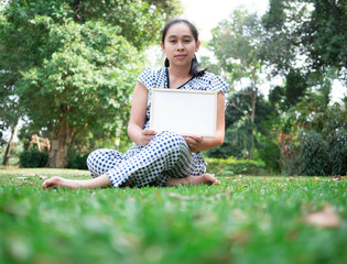 Asian young woman holding blank whiteboard while have pain shoulder and sitting on grass ground in the park. Space for your text.