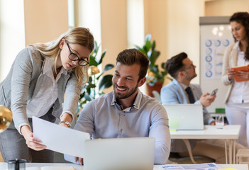 Two young coworkers working together while sitting at the office desk.