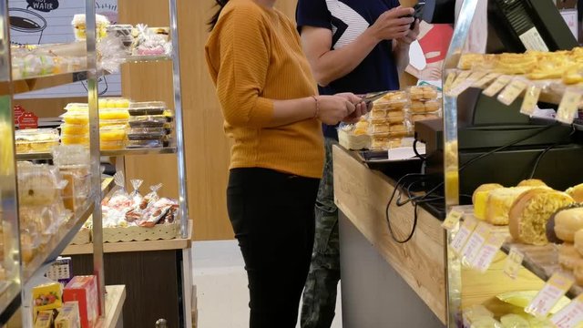 April 2019, Asian young woman in casual clothes is walking in bread shop in the supermarket and pick up bread place down on the tray and walking to pay money at cashier.