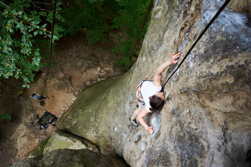 Young female rock climber climbing on cliff with rope. Woman overcoming obstacles on rocks. Extreme summer outdoors on difficult climbing route. Sport in nature. Top view. Success, goal concept.
