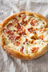 Top view image of cooked pizza with bacon, cheese and thyme served with a glass of wine on white wooden distressed table