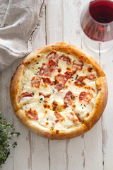 Top view image of cooked pizza with bacon, cheese and thyme served with a glass of wine on white wooden distressed table