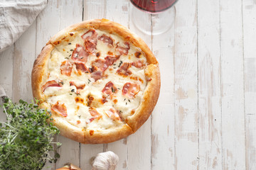 Top view image of cooked pizza with bacon, cheese and thyme served with a glass of wine on white wooden distressed table