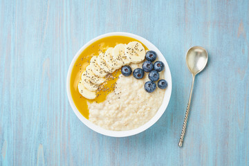 Oatmeal with bananas, blueberries, chia seeds, jam on blue wooden background. Top view. Healthy breakfast.