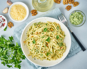 Pesto pasta, bavette with walnuts, parsley, garlic, nuts, olive oil. Top view, close-up, blue background.