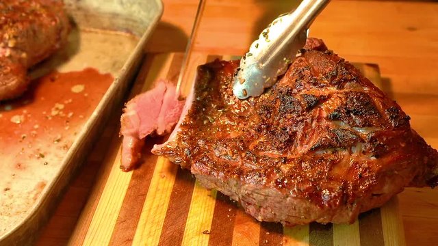 Delicious fatty and juicy lamb meat cooked to rare is being cut with a chef's knife on a wooden cutting board.