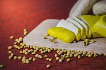 Tofu is sliced on a wooden cutting board and soybean seeds scattered on the table. Healthy food concept.