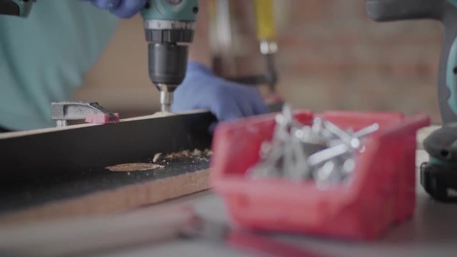 Unrecognized carpenter making halls in the chipboard details with cordless screwdriver. Concept of hand manufacturing. Craftman works in a workshop.