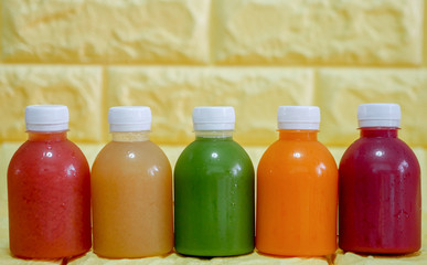 The bottles of cold pressed fruit and vegetables juice with yellow background.