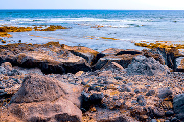 Small stones on a black beach, in the background are akean waves and a surfer