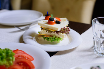 Sandwich with tomato, lettuce, cheese and meat on the white plate