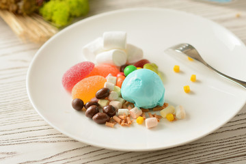gum-flavored ice cream ball with candy and marshmallow decor on a white plate