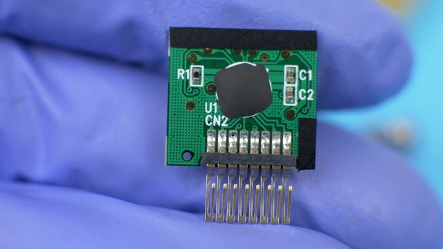 Hand in blue gloves holds electronic green card on blue background with processor. Concept of computer hardware, repairing, upgrade and technology