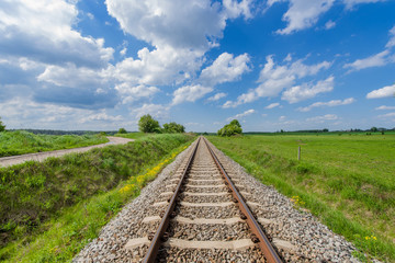 Fototapeta premium Railway traction led straight between green meadows, tracks for a train on the countryside on a background of heaven with beautiful clouds.