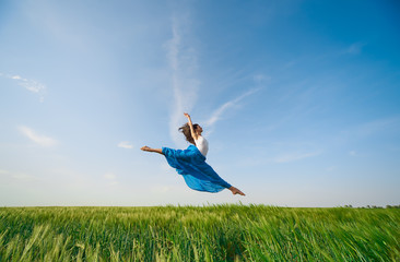 Flying dancer in the air. Happy woman ballerina in blue fabric skirt making a big jump on Green field. Summer or Spring concept  © oes