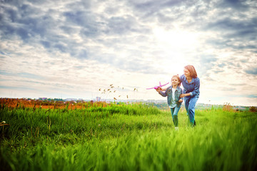Young woman and girl in denim clothes having fun with small plane on green lawn in summer day