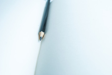 A black pencil lies between the white blank sheets of the sketchbook.