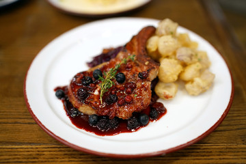 Homemade Pork chop steak with raspberry gravy topped with rosemary leaf, served with sauteed red cabbage and onion fries.