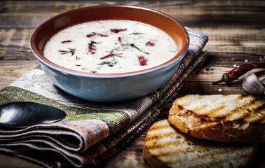 Spicy soup with sour cream, bread and spices on burned wooden table. Traditional rural dinner. Toned