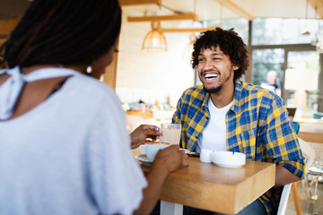 Smiling young african couple sitting at a table at a cafe drinking coffee and talking together