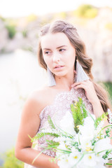 Beautiful young bride with long hair in a wedding dress with a bouquet in the summer on the shore of a beautiful lake