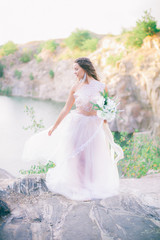 Beautiful young bride with long hair in a wedding dress with a bouquet in the summer on the shore of a beautiful lake
