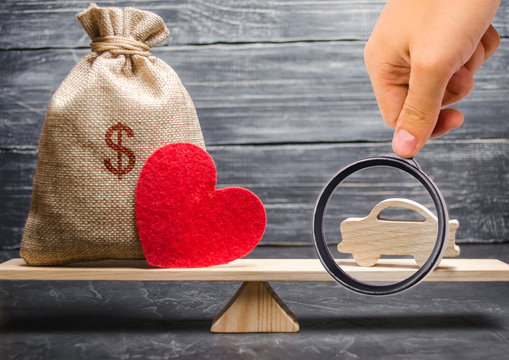 A money bag and a heart with a miniature wooden car on the scales. Auto insurance. Accumulation of money to buy a car. Saving money for a dream. Purchase the auto.