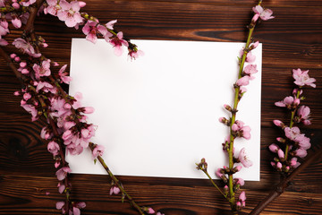 White paper sheet and sprigs of the apricot tree with flowers on wooden background. Place for text. The concept of spring came, happy easter, mother's day.Top view.Flay lay. Copy space.