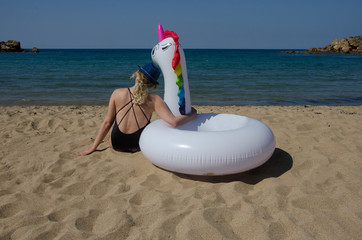 Rear view of woman hugging inflatable unicorn pool float on beach sand near sea