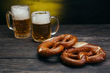 tasty pretzels on dark wooden background with draft beer in the mug in blurred background