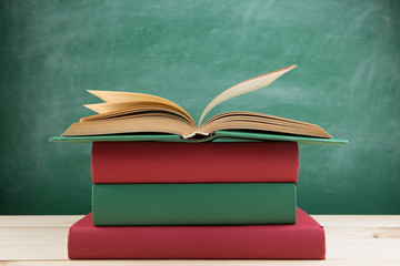Education and reading concept - group of colorful books on the wooden table in the classroom, blackboard background