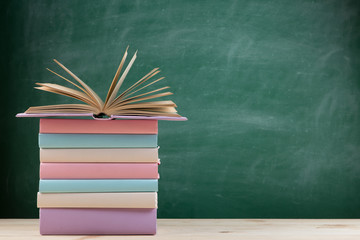 Education and reading concept - group of colorful books on the wooden table in the classroom, blackboard background