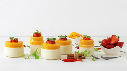 Traditional Italian sweet dessert Panna cotta with mango jelly with touch of red hot chili Piri-Piri served in jars on white wooden table and embellished with fresh real strawberrries and mint.