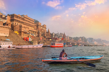 Historic Varanasi city architecture at sunset with view of a boatman rowing on river Ganges