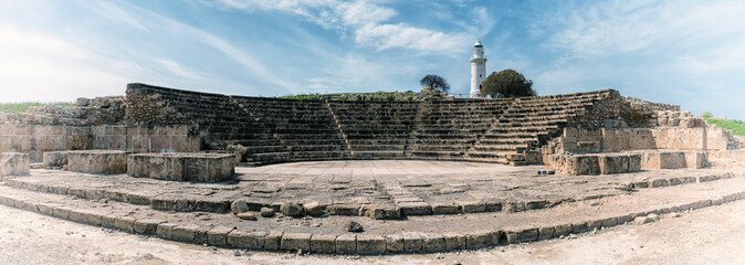 Ancient Odeon amphitheatre in Paphos Archaeological Park (Kato Pafos), harbour of Paphos, Cyprus, panoramic view. Scenic landscape with ruin of medieval architecture, lighthouse and sky, vintage image