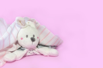 Funny newborn baby toys, teddy hare peeking out from under towel after shower on pink background. Copy space, flat lay, top view.