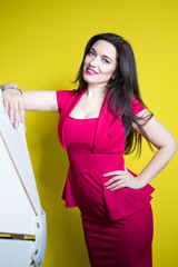  young beautiful woman with long dark hair in a red dress, leans on the furniture on a yellow background