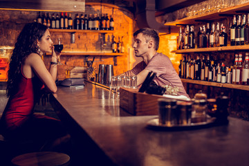 Woman wearing red dress talking to barman and drinking