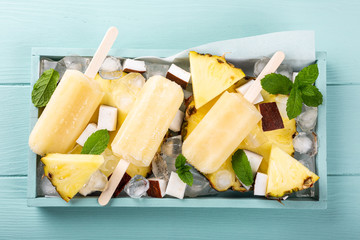 Delicious homemade pineapple coconut popsicles on turquoise background. Summer food concept flat lay. Top view.