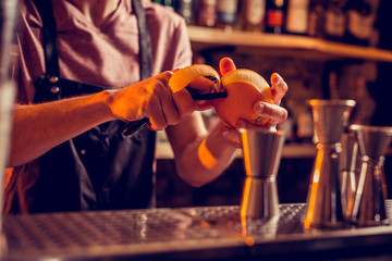 Barman wearing uniform peeling orange for cocktail