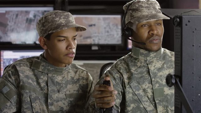 Two military drone operators sitting in front of computer screen talking