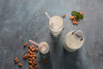 Obraz na płótnie Canvas Almond milk in glass bottles with almonds on background. Vegan diary concept. Healthy food and drinks
