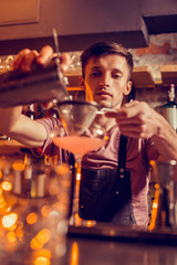 Barman wearing balk apron making cocktail with juice