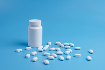 White pills, tablets and white bottle on blue background