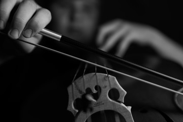 A young cellist practices intensely on his cello, viewed from the bridge and bow side