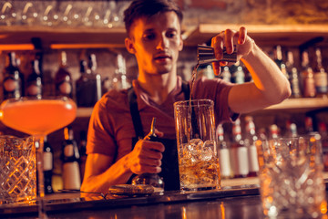 Dark-haired bartender pouring alcohol into glass with ice